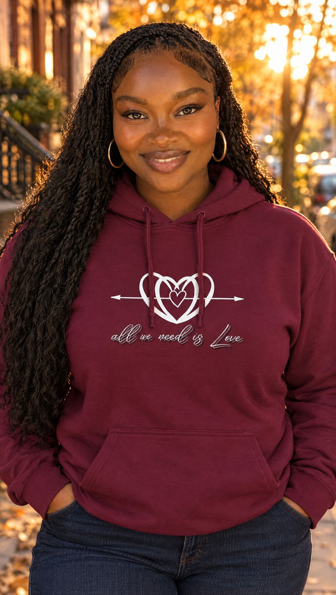 AI-generated model Nia wearing the maroon All We Need is Love hoodie on an autumn street