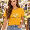 AI-generated model Maya wearing the golden-yellow All We Need is Love crewneck T-shirt at a farmers market